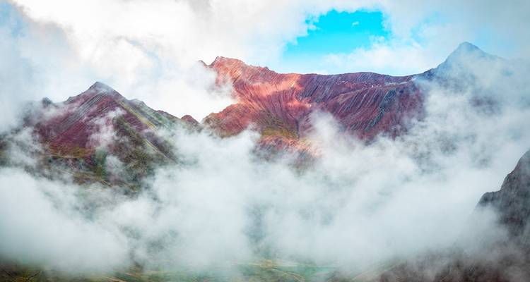 Las nubes se arremolinan alrededor de picos andinos dentados y coloridos con un rayo de luz solar abriéndose paso.