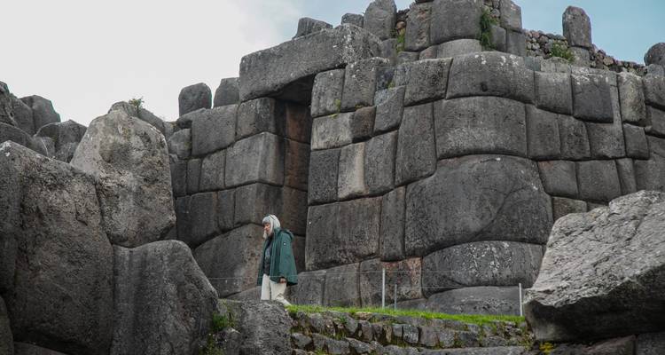 Visitante con poncho verde parado bajo las masivas murallas de piedra ciclópeas de Sacsayhuamán