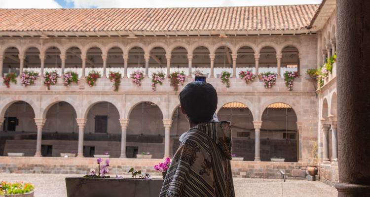 Visitante tomando una foto móvil de un patio claustral adornado con macetas colgantes