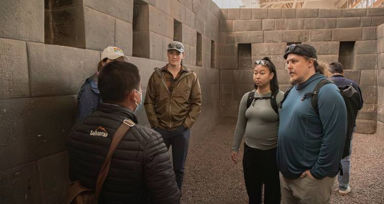 Guía explicando la cantería dentro de una sala del templo inca poco iluminada a un pequeño grupo de turistas
