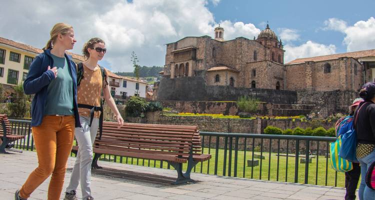 Dos mujeres paseando por un malecón con el complejo Qorikancha detrás de ellas en un día luminoso