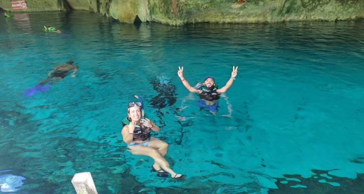 Reisende treiben im Wasser und zeigen Peace-Zeichen beim Schnorcheln in den kristallklaren türkisfarbenen Gewässern einer Cenote.