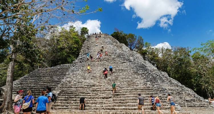 Besucher erklimmen die steile antike Steinpyramide von Coba unter einem strahlend blauen Himmel.