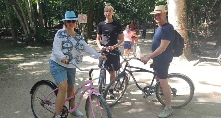 Familiengruppe mit Fahrrädern macht Pause auf einem schattigen Erdweg in den Dschungelruinen von Coba.