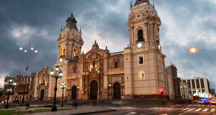 Evening view of Lima Cathedral illuminated against a moody sky on the main square.