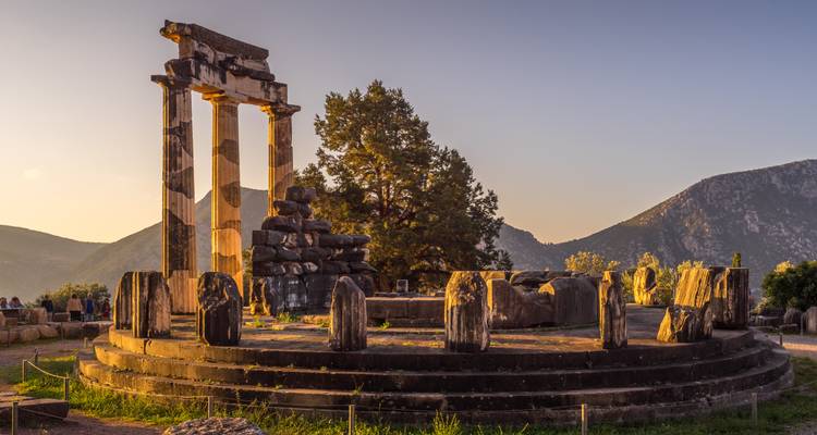 La lumière dorée du coucher de soleil baigne la Tholos circulaire de Delphes et l'arrière-plan montagneux environnant.