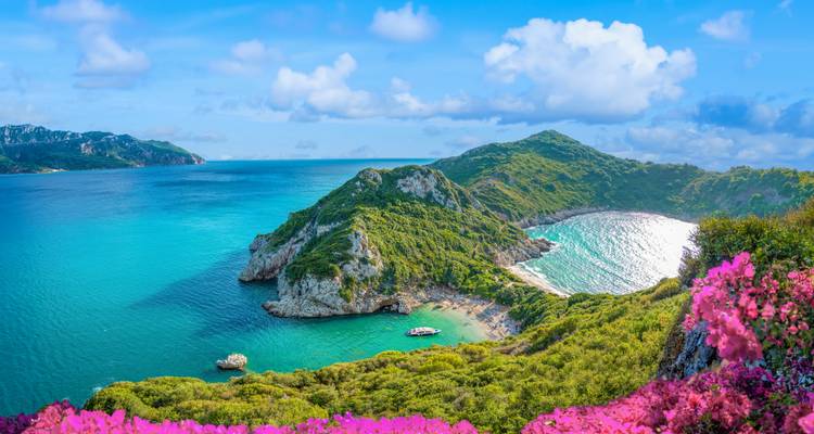 Vue aérienne saisissante de la double baie de Porto Timoni à Corfou encadrée par des fleurs rose vif et une mer turquoise.