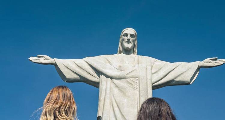 Deux visiteurs lèvent les yeux vers l'emblématique statue du Christ Rédempteur sur fond de ciel bleu éclatant.