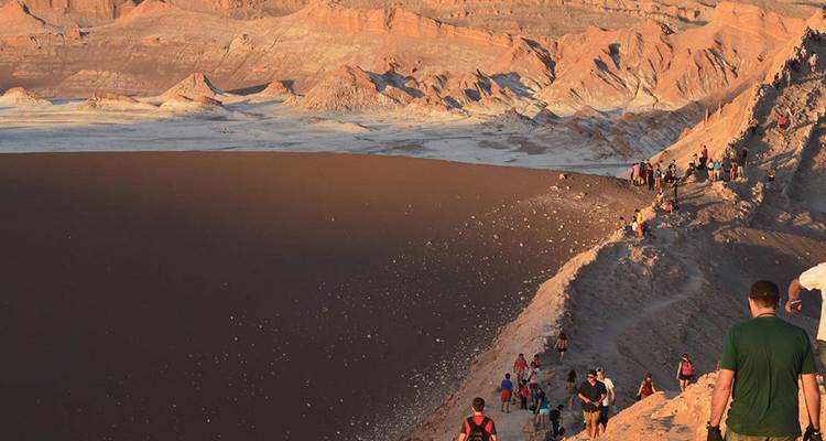 Long line of visitors hiking along the dramatic rim of Valle de la Luna with multicoloured desert formations.