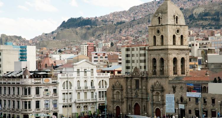 Colonial stone church and city buildings set against a hillside densely covered with homes in La Paz.