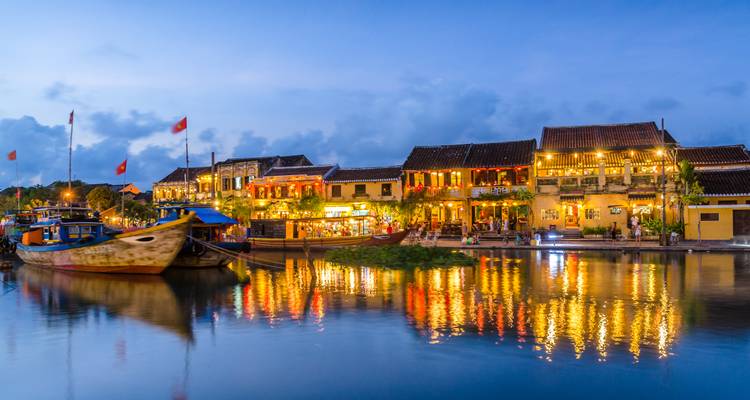 Laternen-beleuchtete historische Flussufergebäude spiegeln sich in ruhigen Gewässern zur blauen Stunde in Hoi An wider.