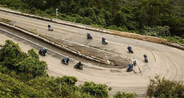 Un convoi de motocyclettes s'incline dans un virage en épingle à cheveux spectaculaire couvert de jungle sur une route de col de montagne