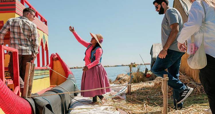 Une femme locale salue les visiteurs qui montent à bord d'un bateau en roseaux aux couleurs vives sur les îles Uros du lac Titicaca.