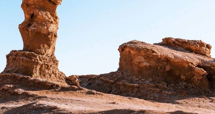 Formaciones de arenisca erosionada se alzan desde un árido paisaje desértico de color oxidado bajo un cielo despejado en el Atacama.