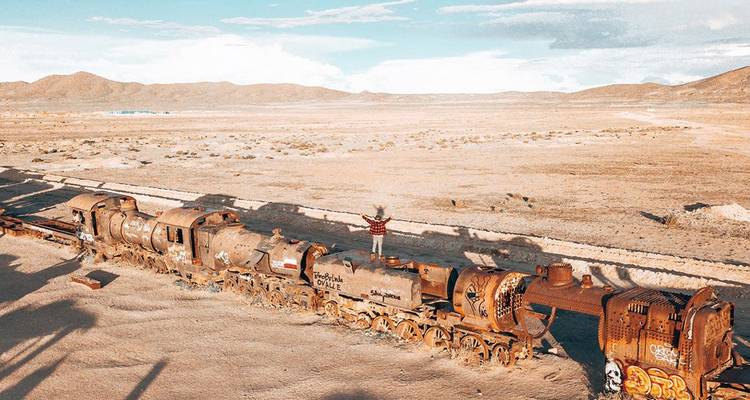 Vue aérienne des locomotives rouillées au Cimetière des Trains d'Uyuni avec un voyageur solitaire debout au sommet.