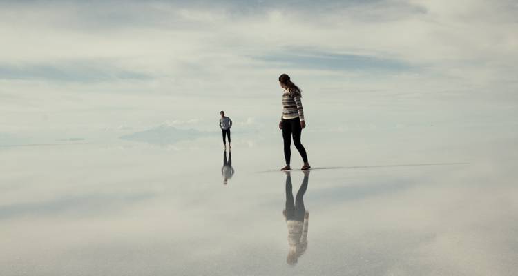 Deux voyageurs marchent sur la surface réfléchissante du Salar d'Uyuni créant des images miroir parfaites.