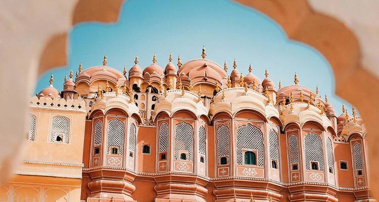 La façade ornée du Hawa Mahal de Jaipur encadrée par une fenêtre en arc contre un ciel turquoise.