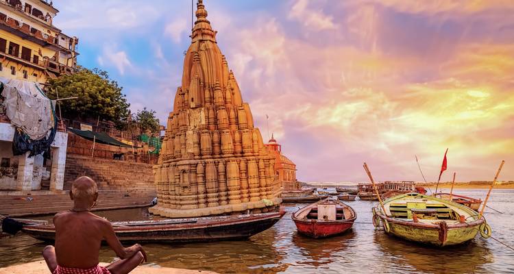 Torre del templo de tonos dorados en el Ganges con botes coloridos y cielo dramático de atardecer en Varanasi.