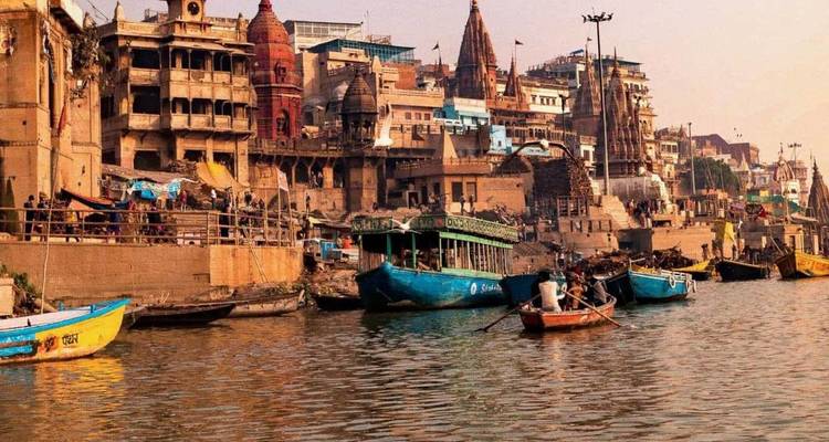 Historische ghats van Varanasi met kleurrijke gebouwen aan de rivier en houten boten op de Ganges bij zonsopgang.