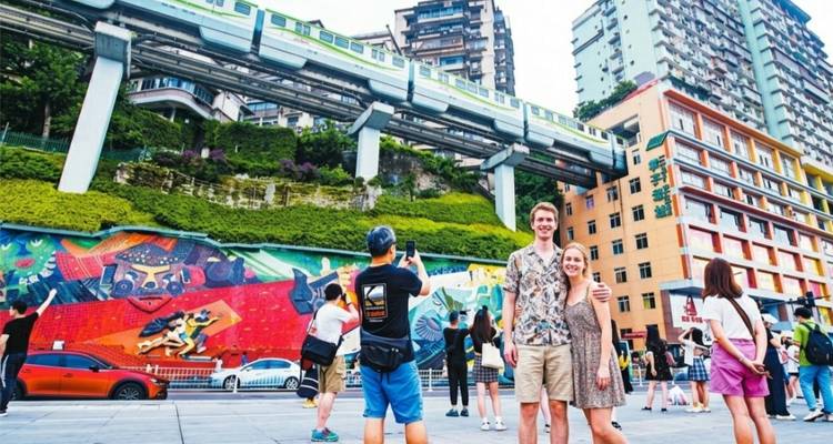 Les touristes posent sous la voie de monorail surélevée de Chongqing et la fresque d'art urbain colorée.