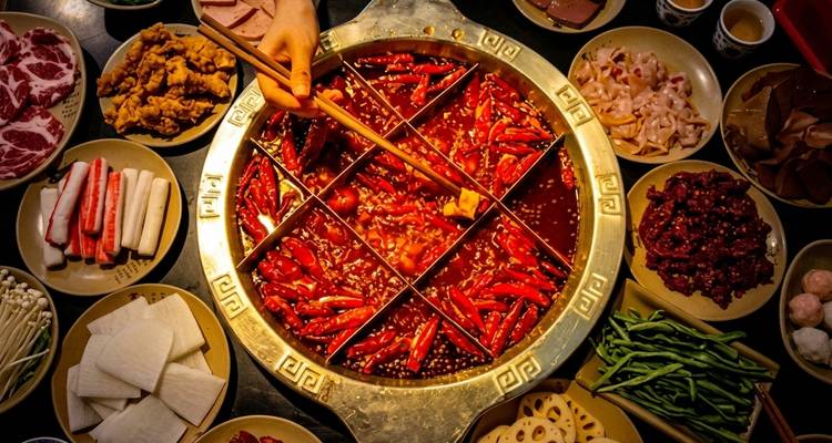 Plan en plongée d'un hotpot de Chongqing fumant divisé en sections épicées entouré d'ingrédients crus.
