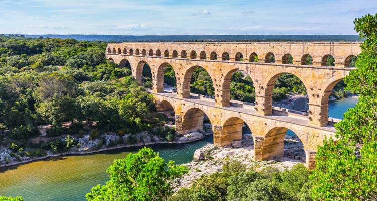 Ancient three-tier Pont du Gard aqueduct spans a river valley surrounded by forest.