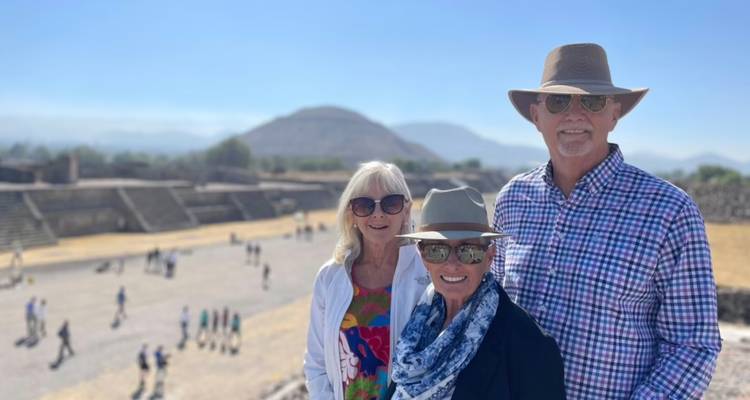Trois voyageurs souriants posent devant l'ancienne place et les pyramides de Teotihuacan par une belle journée ensoleillée.