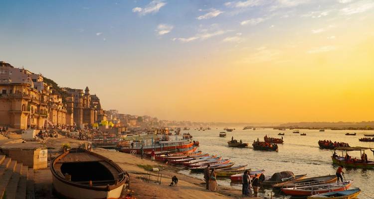 Boote und Ghats entlang des Ganges in Varanasi bei goldenem Sonnenaufgang mit Pilgern und Einheimischen.