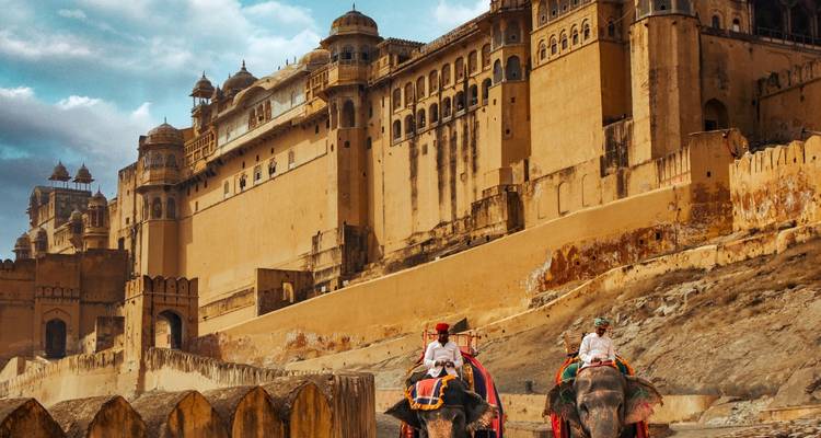 Touristen reiten auf geschmückten Elefanten die Festungswalle von Amber Fort unter einem stimmungsvollen Himmel hinauf