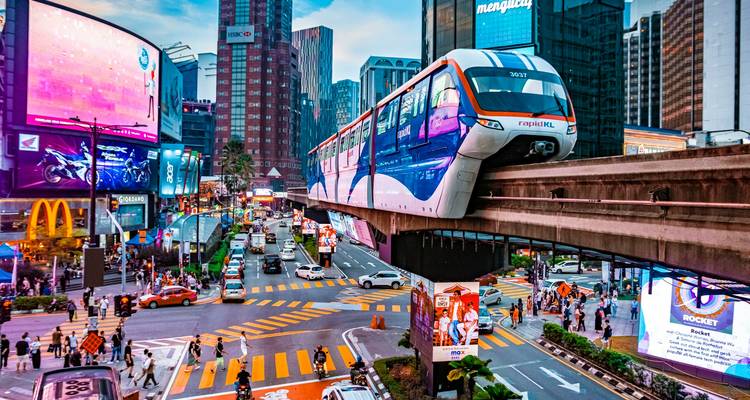 Vibrante intersección de Bukit Bintang con monorraíl deslizándose sobre vallas publicitarias de neón y tráfico bullicioso.