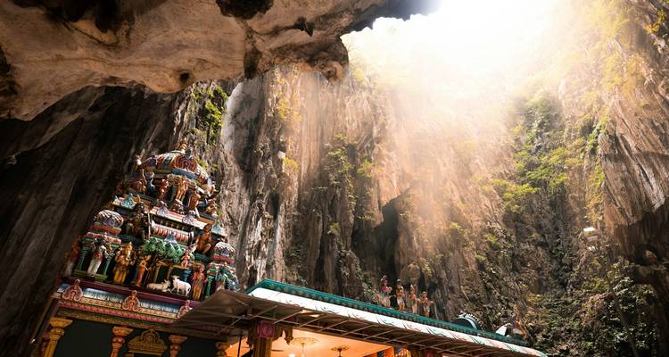 Los rayos del sol se derraman en las Cuevas Batu iluminando un vívido santuario hindú contra imponentes paredes de piedra caliza