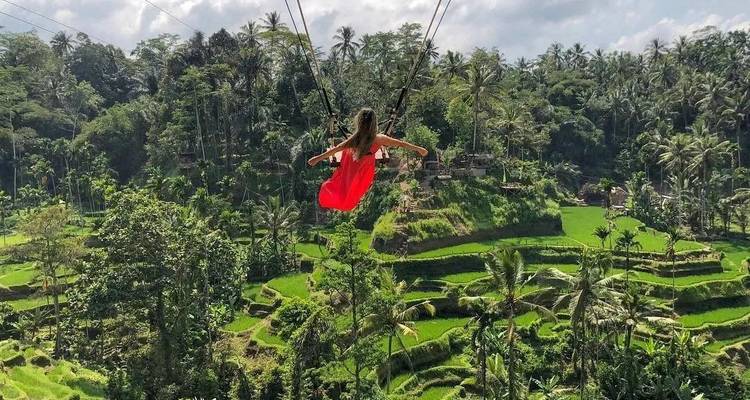 Mujer en un vestido rojo volando en un columpio de la selva sobre vibrantes terrazas de arroz escalonadas en Bali.