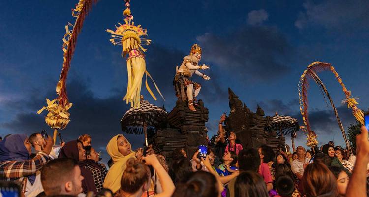 Actuación vespertina de Kecak con un bailarín disfrazado interactuando con la multitud bajo un cielo dramático del crepúsculo.