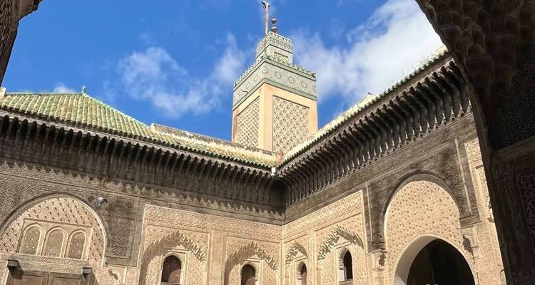 Intricately carved courtyard and minaret of a historic madrasa under a vivid blue sky.