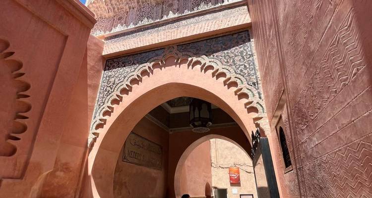 Ornate pink-plastered archway with carved detailing leading into a historic Moroccan complex.