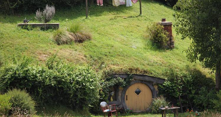 Grassy hillside with a round yellow Hobbit hole door, washing line and lush garden in Hobbiton.