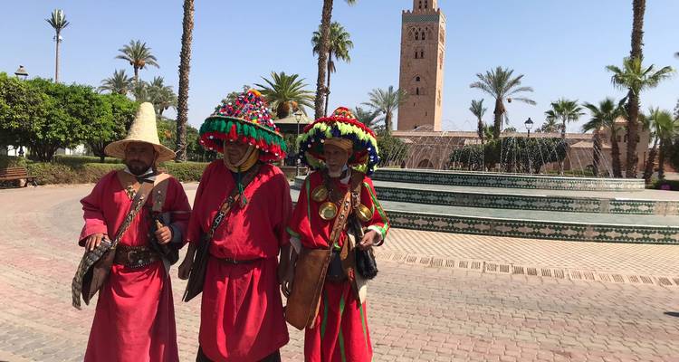 Tres vendedores de agua marroquíes con trajes coloridos cerca de una fuente y la Mezquita Kutubía.