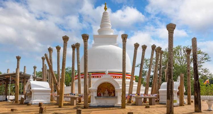 Un stupa blanc brillant entouré de hautes colonnes de pierre s'élève dans un ciel bleu dans un ancien temple sri-lankais.