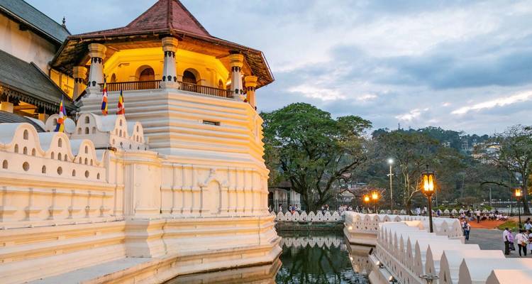 Les façades blanches du Temple de la Dent sont éclairées par des lampes chaleureuses près du lac Kandy au crépuscule.