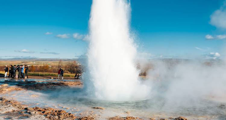 Krachtige Strokkur geiser barst uit met een torenhoge kolom van water en stoom terwijl toeristen vanaf veilige afstand toekijken