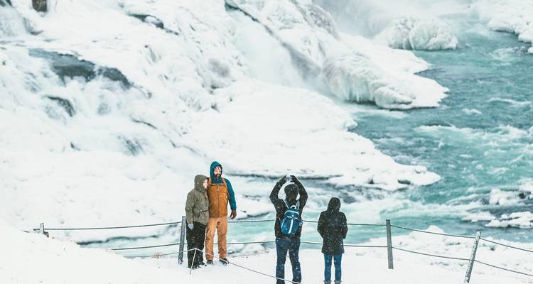 Vier toeristen poseren voor de ijzige turquoise cascades van Gullfoss tijdens een sneeuwstorm
