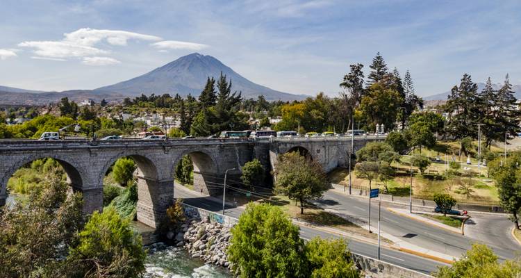 Un vieux pont de pierre enjambe une rivière avec le volcan Misti au sommet enneigé et de forme conique qui s'élève au-dessus de la ville d'Arequipa.