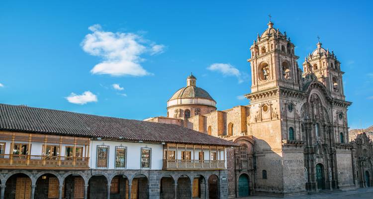 La lumière matinale baigne l'église La Compañía de Cusco et l'arcade coloniale sous un ciel d'un bleu éclatant.