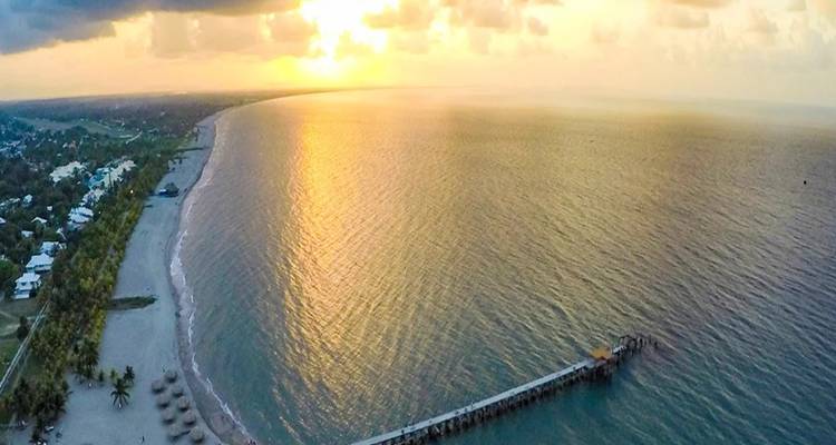 Wide aerial panorama of a long sandy coastline and pier glowing in warm sunset light.