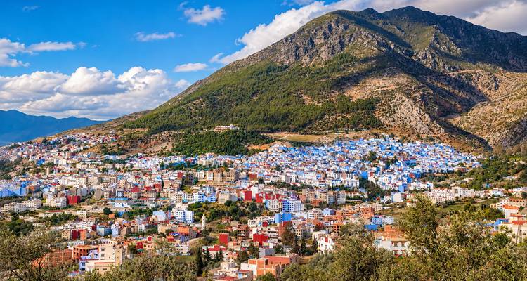 Vista panorámica de las casas azules de Chefchaouen extendiéndose por la ladera de la colina bajo un pico escarpado.