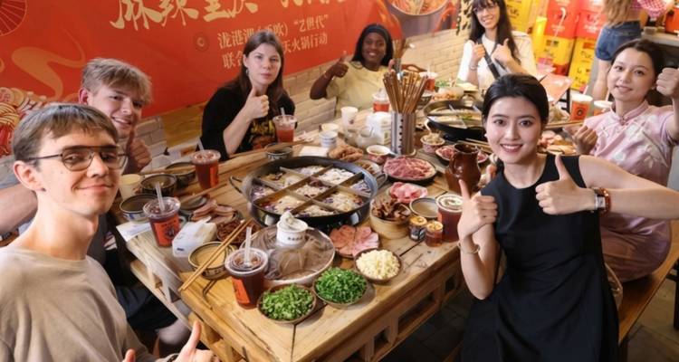 Smiling international friends give thumbs up around a steaming hotpot feast in a casual Chinese restaurant.