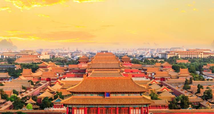 Panoramic aerial of Beijing’s Forbidden City bathed in warm sunset light with city skyline behind.