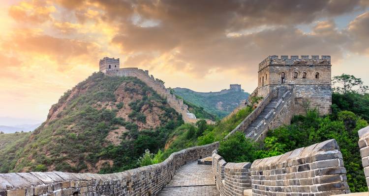 Great Wall of China snaking over lush mountain ridges under a dramatic golden sky.