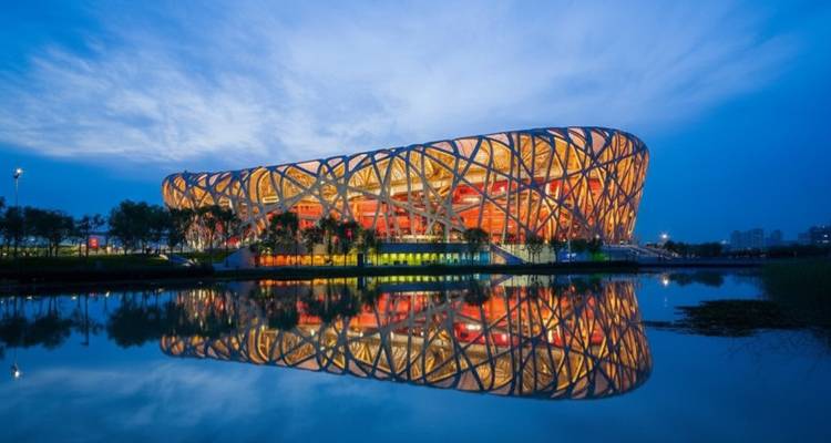 Beijing’s Bird’s Nest Stadium illuminated at dusk, reflecting perfectly in still water.