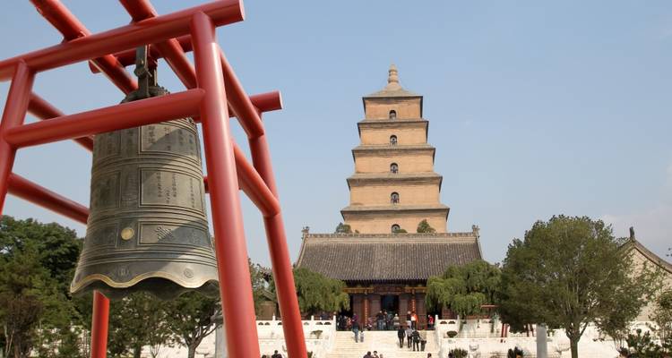Ancient bell in foreground with Xi’an’s Big Wild Goose Pagoda rising behind against blue sky.